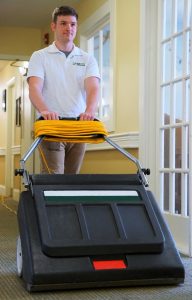 Flexgreen employee vacuuming a senior living home hallway with a commercial vacuum cleaner