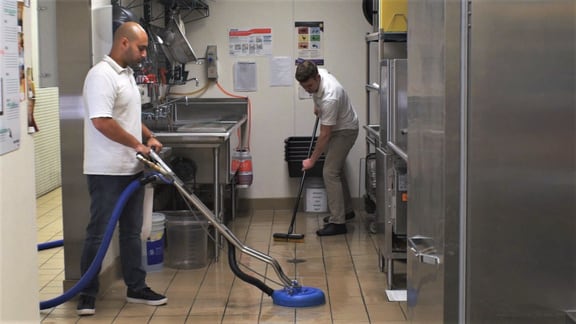 Two Flexgreen employees cleaning and degreasing a commercial restaurant kitchen flooring