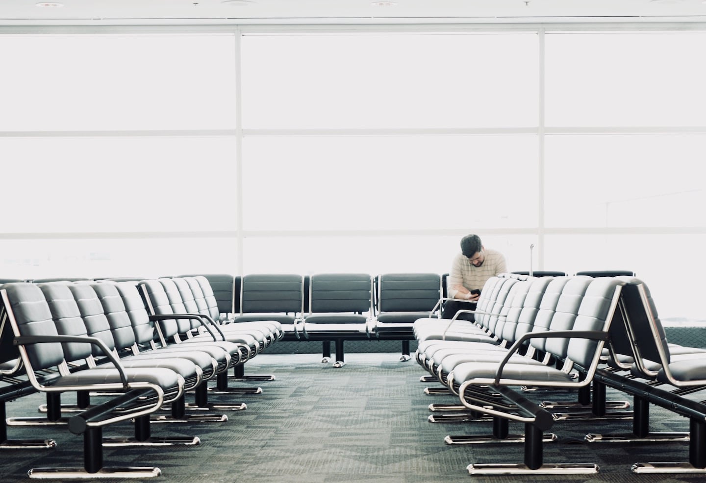 An RDU airport gate seating area that has a carpet. One man waits against the windows for his flight.