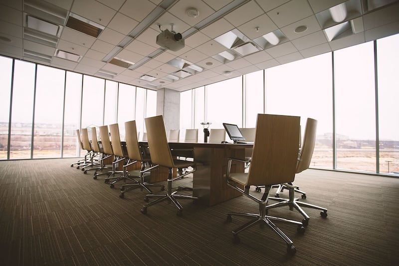 An empty corner, corporate office conference room with carpeting and floor to ceiling windows overlooking a city